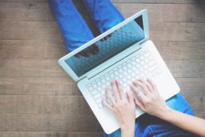 A woman works on a small white laptop on her lap.