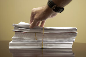 A man's hand flips through a large stack of papers secured by rubber bands